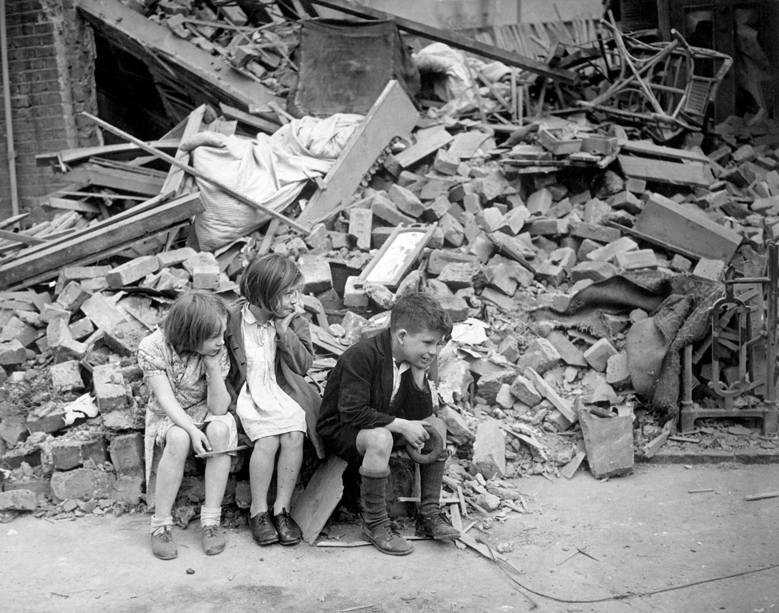 children sitting outside bombed house